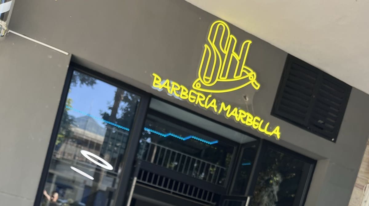 Fachada de SH Barbería con el rótulo de neón y un cliente con diseño a navaja